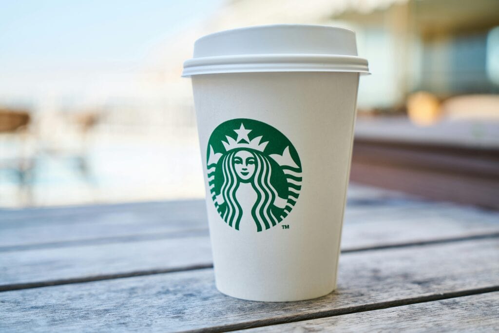 Close-up of a Starbucks coffee cup with the iconic green logo, held by a person in a casual setting