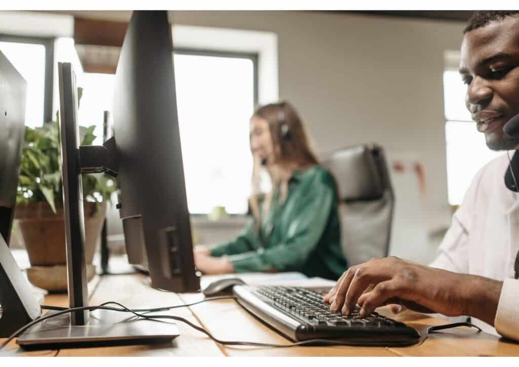 Two digital agency professionals working at desktop computers with headsets in a bright modern office environment